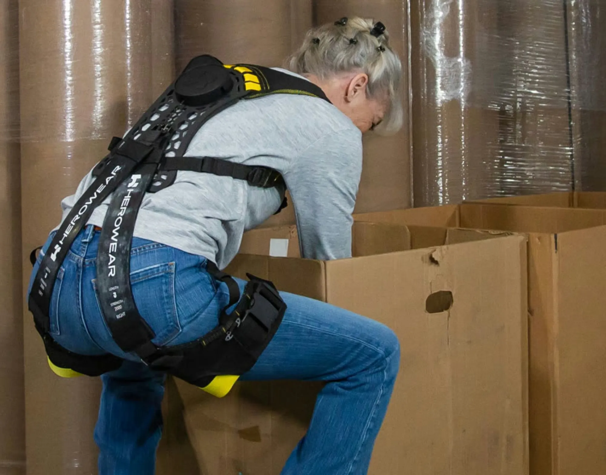 A grocery distribution centre worker wearing the Apex 2, bending to lift from a carton