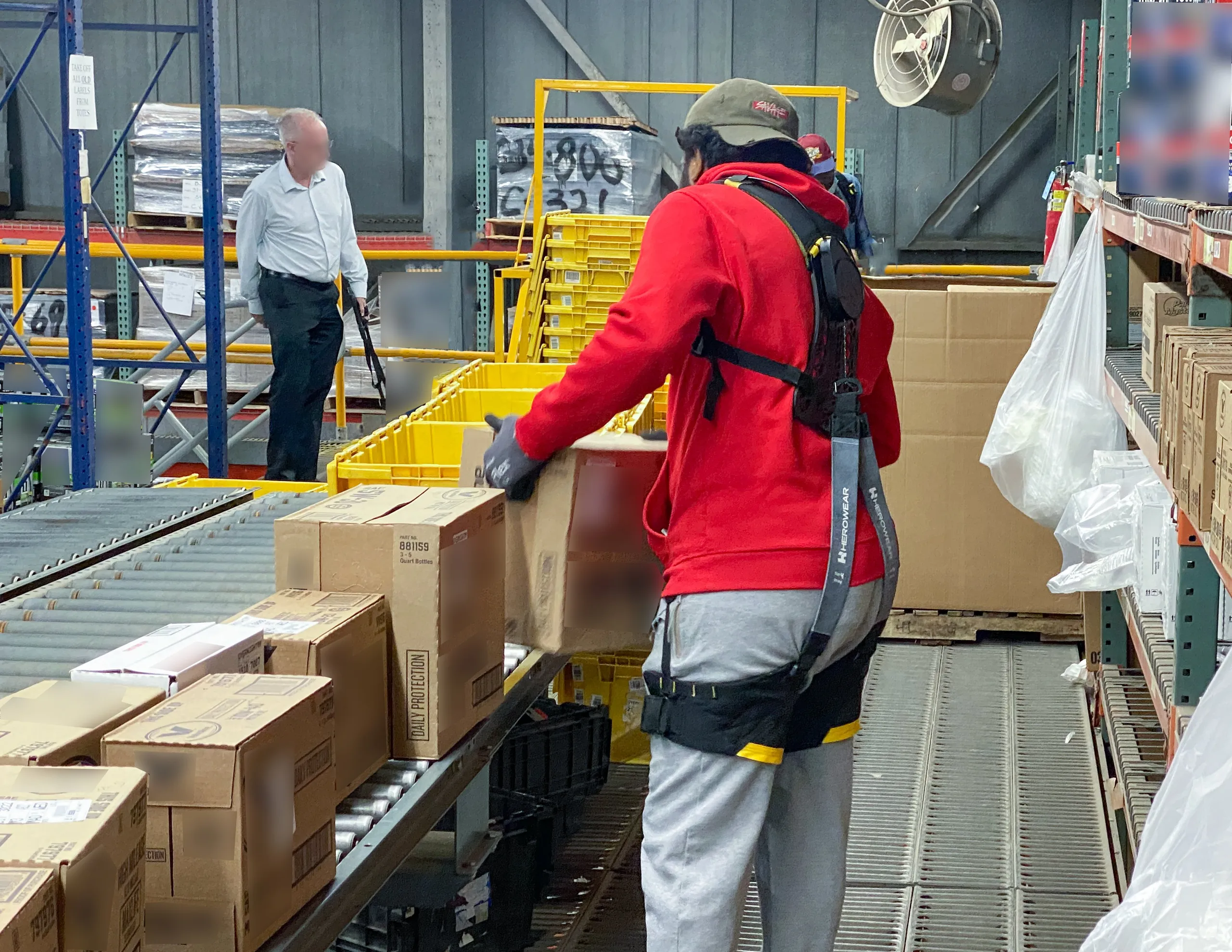 A distribution centre worker in a red top wearing the Apex 2, moving cartons along a conveyor line