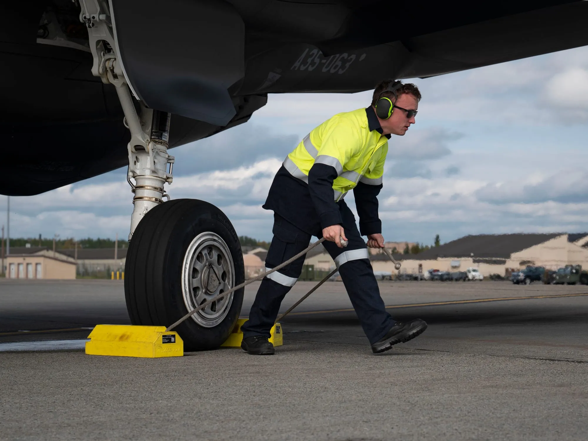 A Royal Australian Air Force aircraft technician in hi-vis pulling the wheel chocks from under an F-35A on the flight line