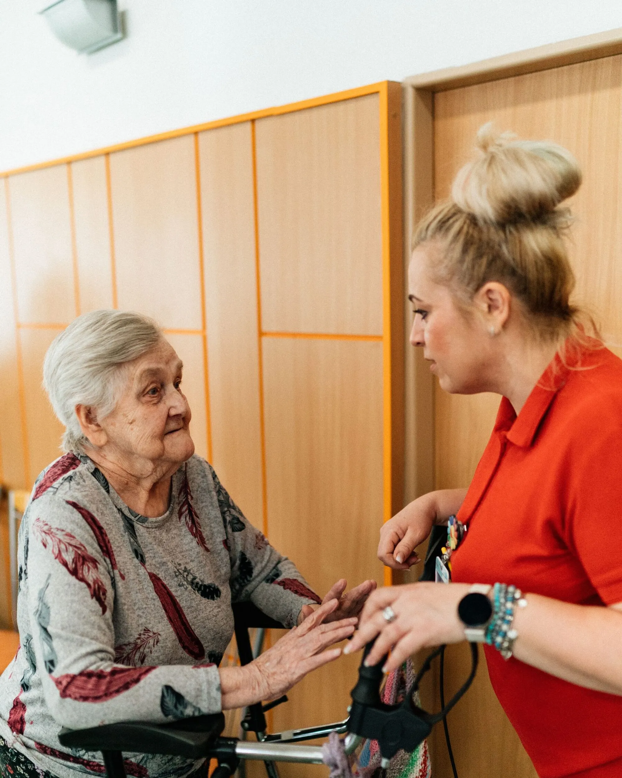 A care worker steadying an older woman at her walking frame in a care home corridor