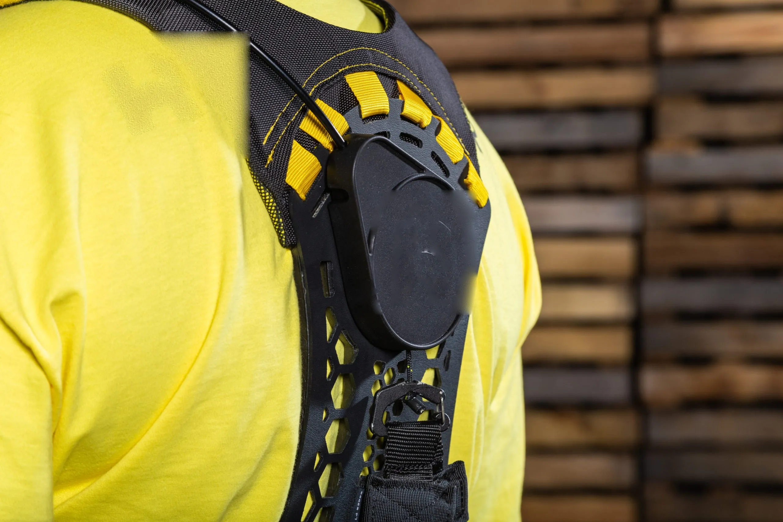 A worker in a yellow hi-vis shirt wearing the Apex 2, the black and yellow back unit filling the frame, in a timber yard