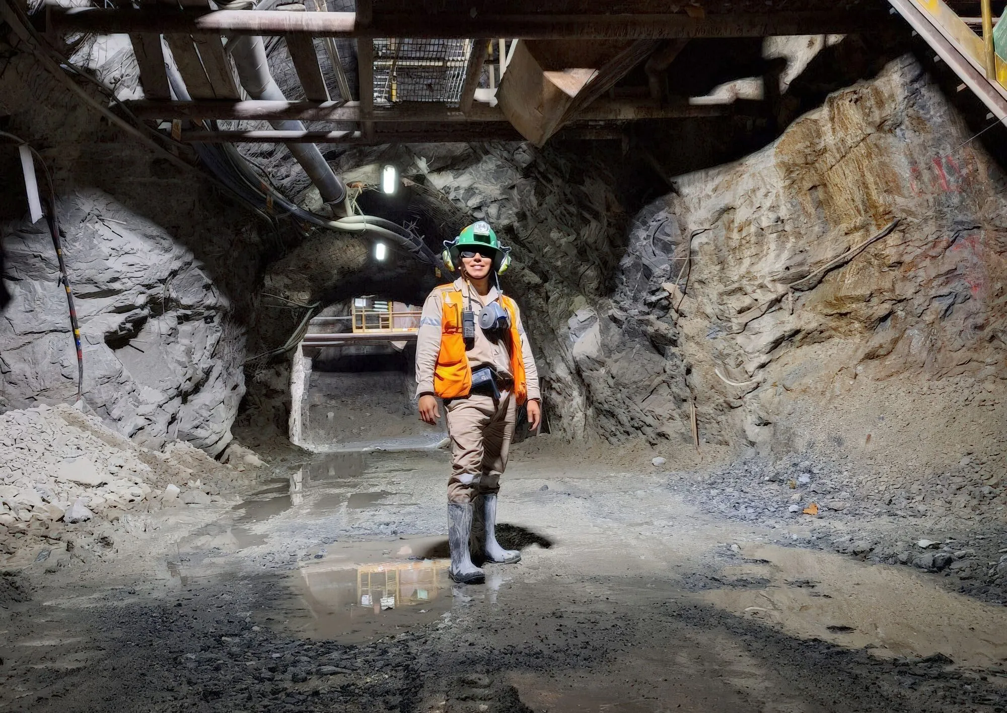 A miner in hi-vis and a lamped hard hat standing in an underground drive below a steel work platform