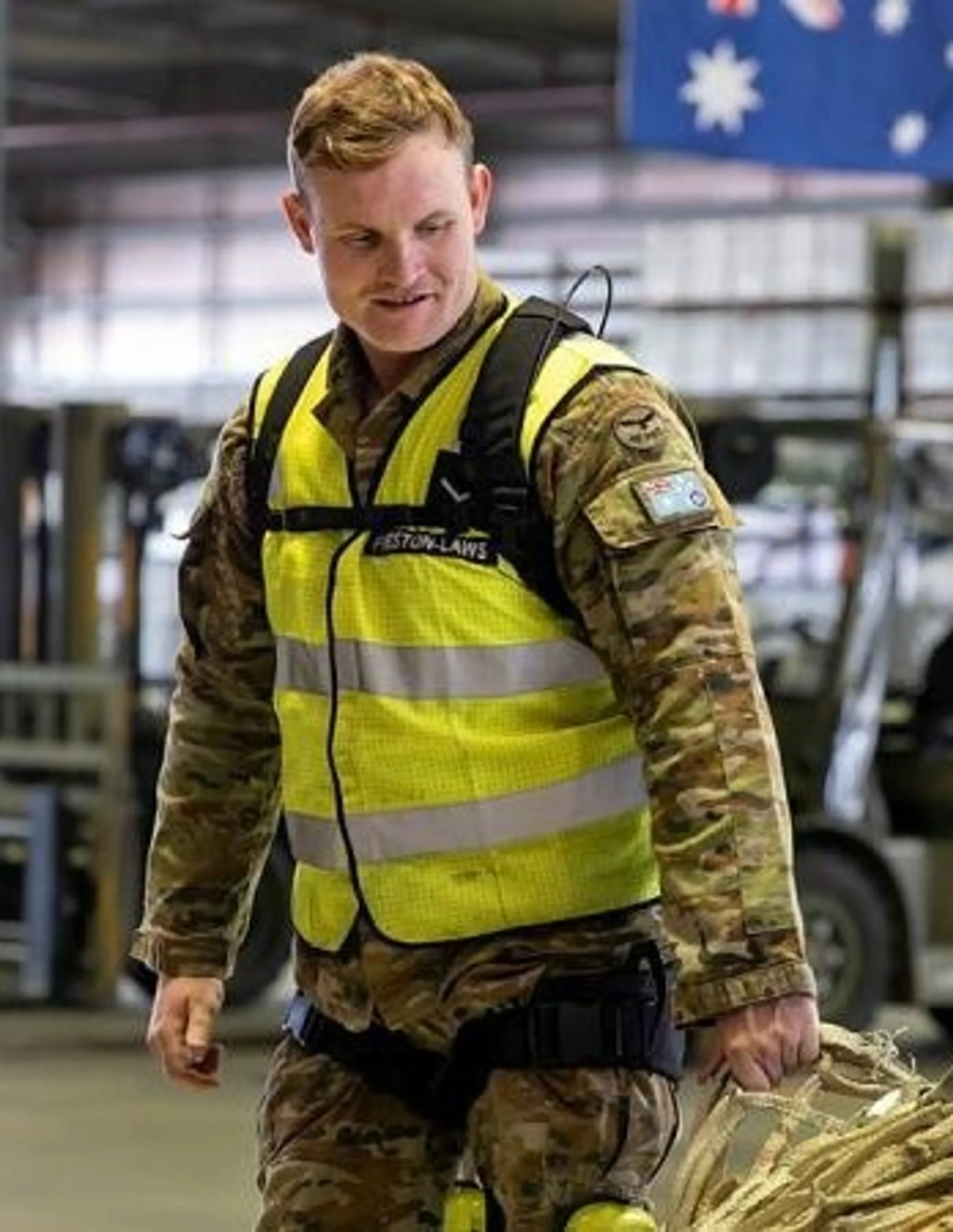 An air force member in camouflage uniform and a hi-vis vest wearing the Apex 2 in a hangar