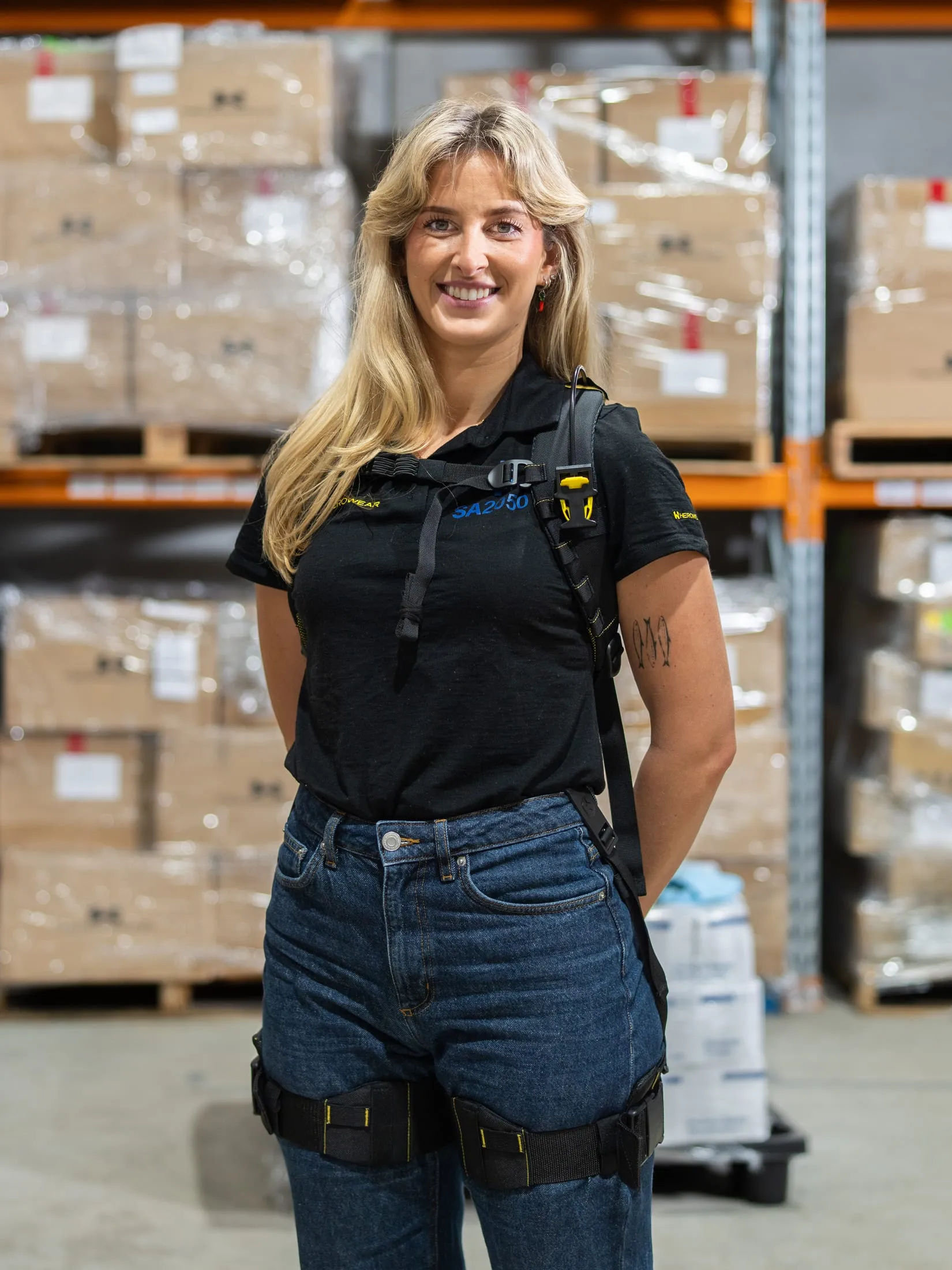 A worker in a black SA2050 polo shirt and the Apex 2, standing in front of racked and shrink-wrapped pallets